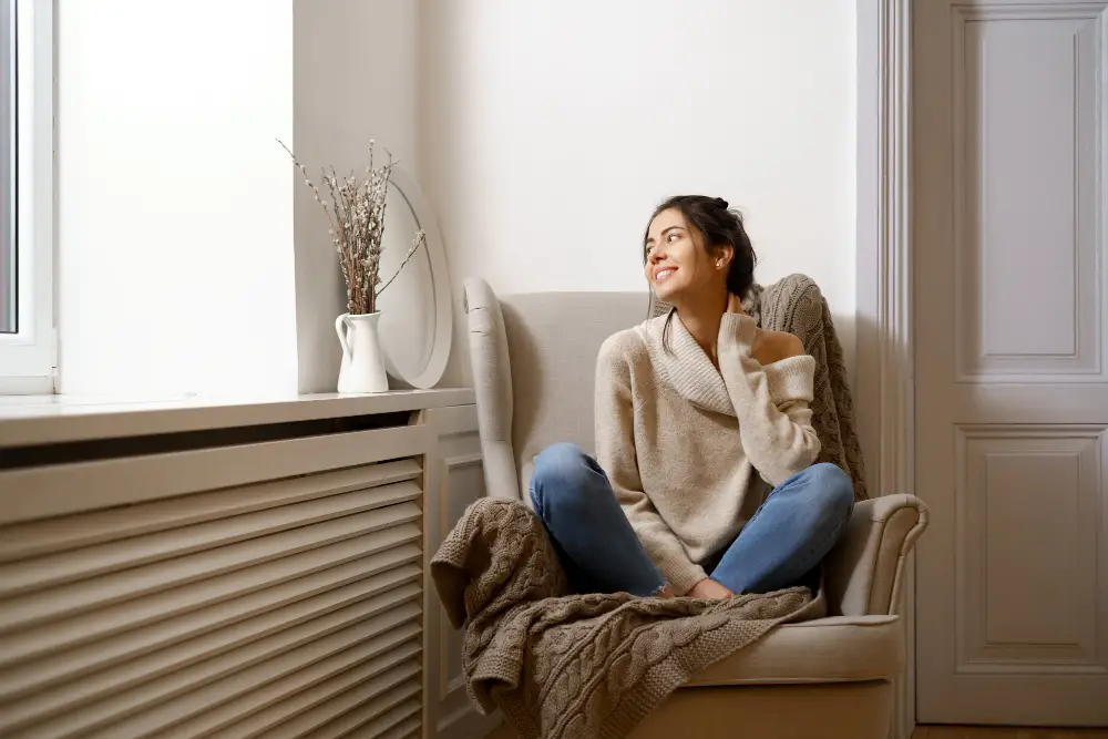 A lady smiling and staying warm next to her high efficiency electric radiator supplied by Cotswold Electric Heating.