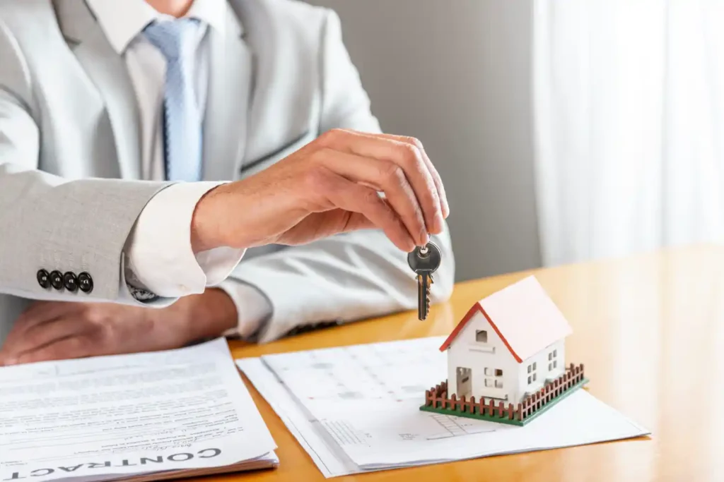 An image of someone handing over some keys in front of a miniature house to show the topic of the blog post: electric heating for landlords: low maintenance heating for rental properties.